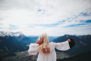 Blonde woman in a white dress overlooks the beautiful mountain landscape of Ohlstadt, Germany.